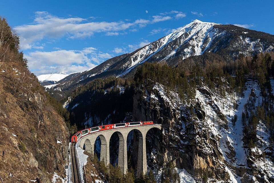 A red train crossing the Landwasser Viaduct into the cliff tunnel