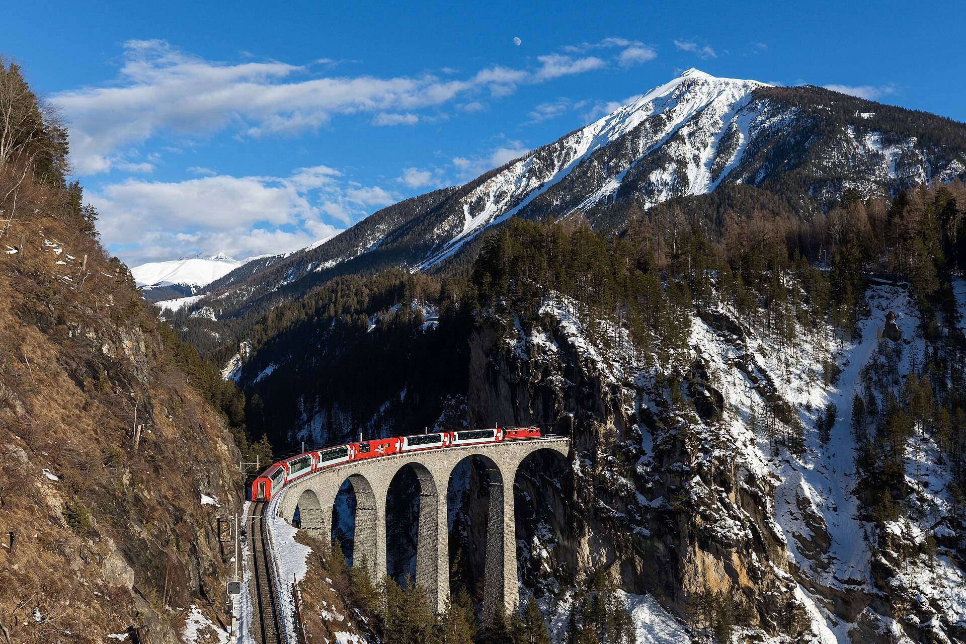 A red train crossing the Landwasser Viaduct into the cliff tunnel